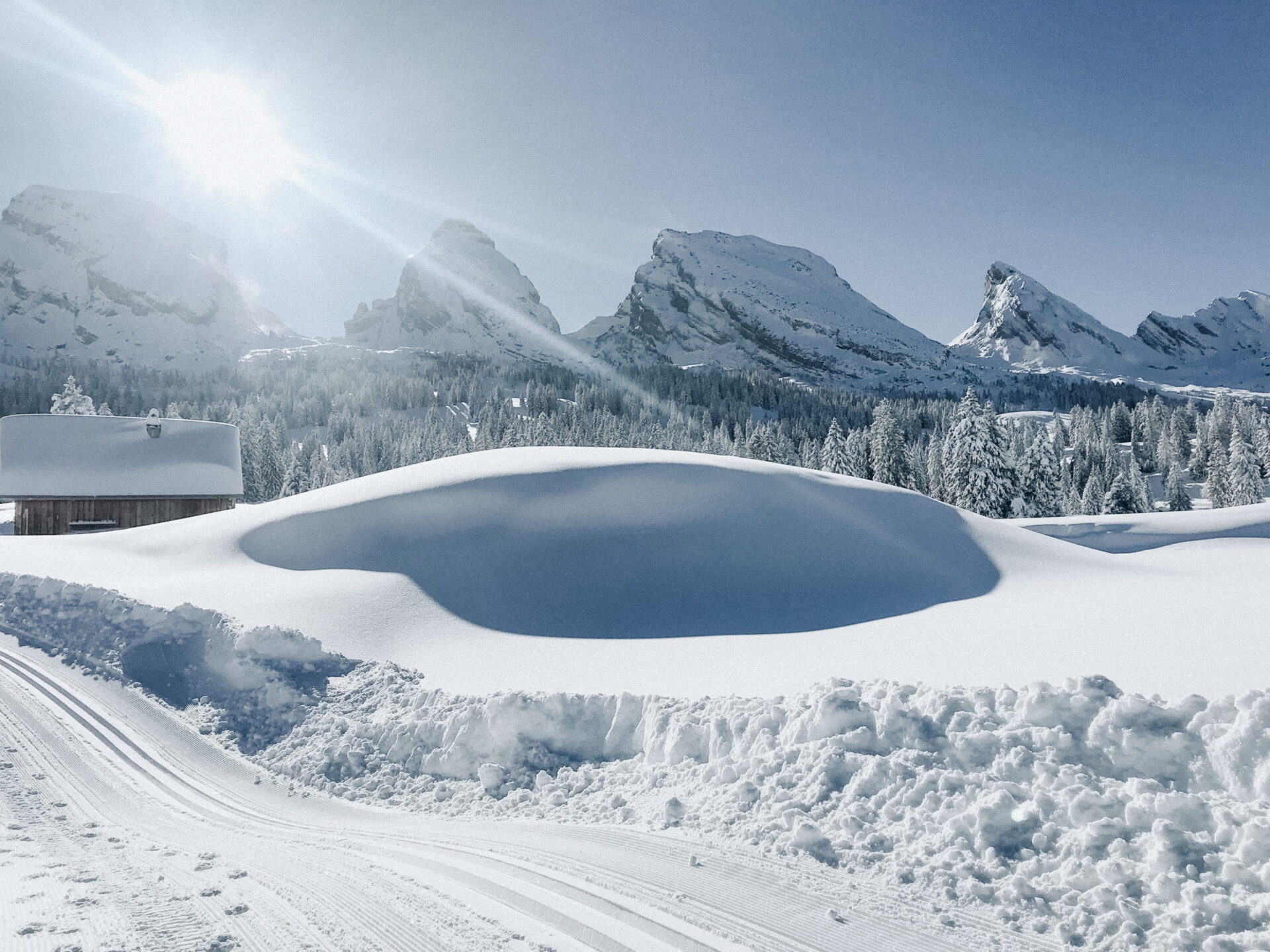 Winterwandern im Toggenburg mit Blick auf die Churfirsten und grossem Schneehügel mit Holzhütte im Hintergrund