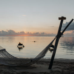 Sonnenuntergang am Strand von Lux Le Morne mit Hängematte im Vordergrund, auf dem Wasser schwimmen Feuerstellen