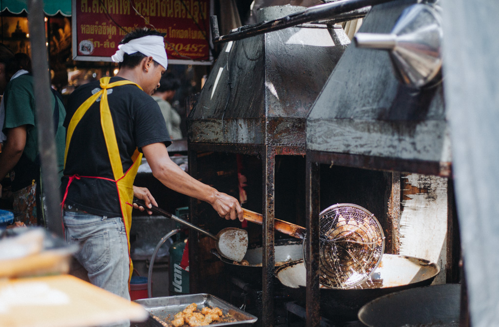 Street Food Stände sind in Bangkok ganz normal und hier gibt es das beste Essen, ein Mann frittiert gerade Essen in einem riesigen Wok auf dem Chatuchak Markt in Bangkok