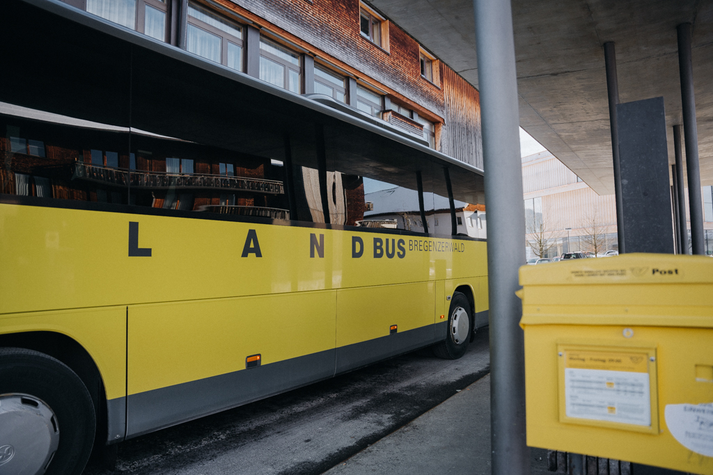 Blick auf den gelben Landbus im Bregenzerwald an der Haltestelle Hittisau Dorf mit gelbem Briefkasten im Vordergrund
