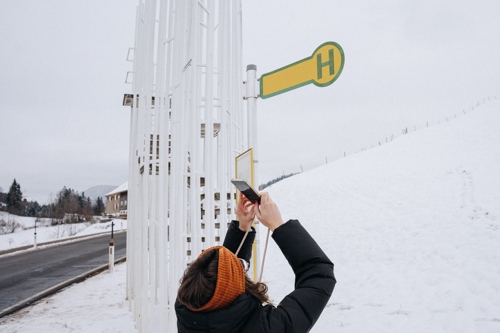 Bushaltestelle mit Haltestellenschild, eine Frau fotografiert in den Himmel und macht ein Foto mit ihrem Smartphone in Krumbach
