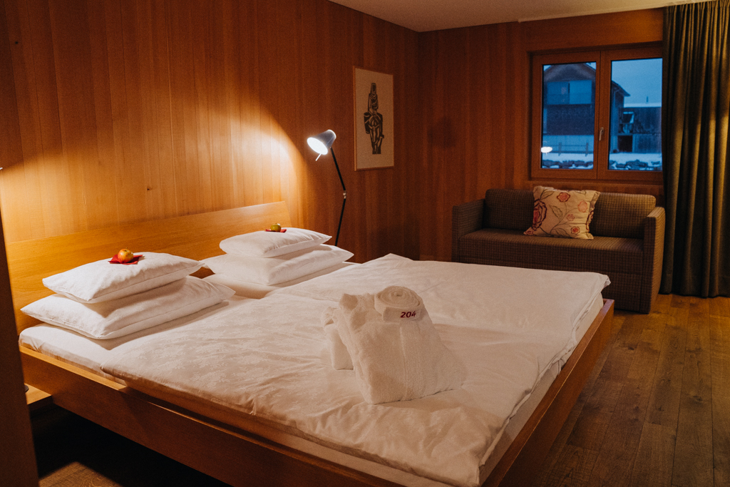 Blick auf das Bett im Bregenzerwald Zimmer im Hotel Krone Hittisau mit frischen Äpfeln auf den Kopfkissen