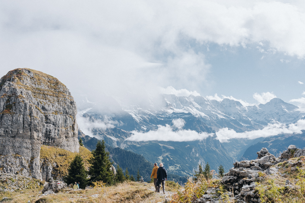 zwei Wanderer auf der Wanderung auf der Schynige Platte beim Aussichtspunkt Daube laufen in Richtung Bahnhof mit Panorama der Alpen im Hintergrund mit Sicht auf Eiger, Jungfrau und Mönch in der Jungfrau Region