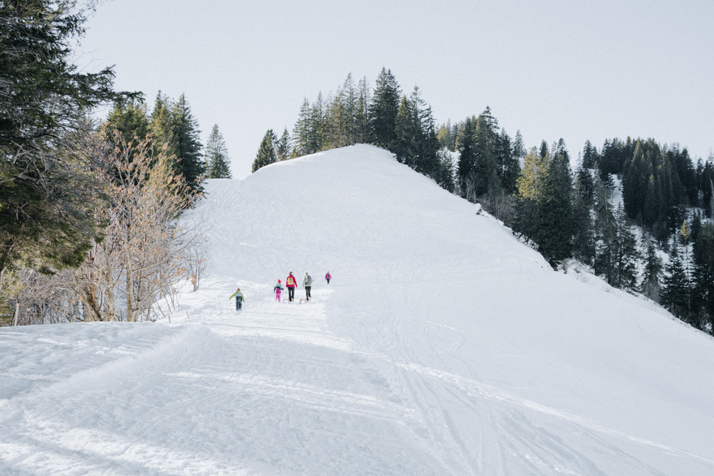 Winterwandern in der Schweiz mit viel Schnee, Familie stapft auf dem präparierten Winterwanderweg