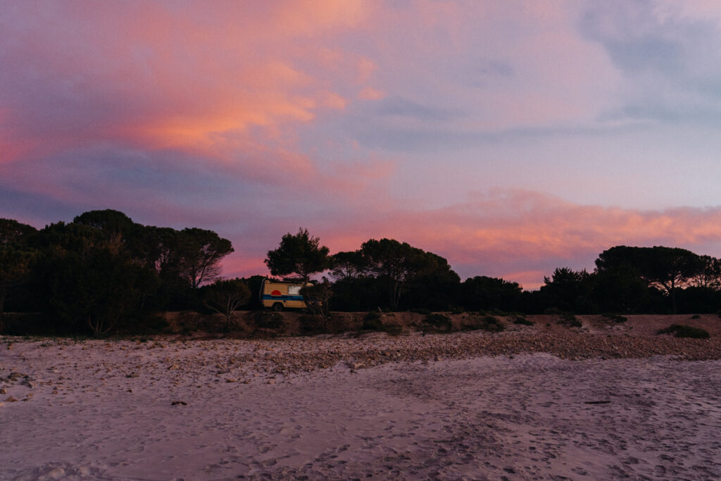 Camper Hubi am Stellplatz bei rosa Sonnenuntergang am Strand auf der Sardinien Rundreise